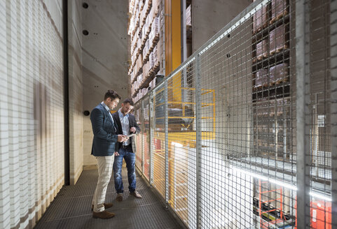 Two men in automatized high rack warehouse looking at tablet - DIGF01782