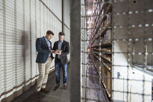 Two men in automatized high rack warehouse looking at tablet - DIGF01787