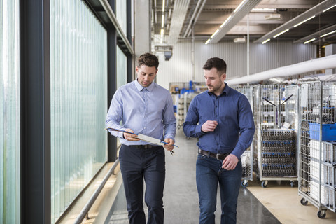 Two men walking in factory shop floor talking about product stock photo