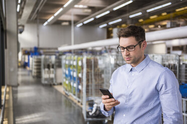 Geschäftsmann in der Fabrikhalle schaut auf sein Handy - DIGF01837