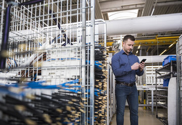 Geschäftsmann in der Fabrikhalle schaut auf sein Handy - DIGF01838