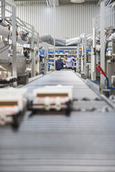 Two men talking at conveyor belt in factory shop floor - DIGF01845