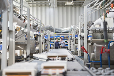 Two men talking at conveyor belt in factory shop floor - DIGF01846