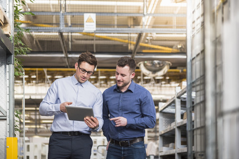 Zwei Männer mit Tablet im Gespräch in einer Fabrikhalle, lizenzfreies Stockfoto