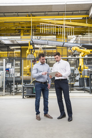 Two men with tablet talking in factory shop floor stock photo