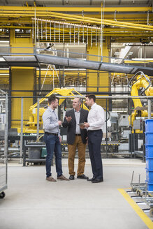 Three men with tablet talking in factory shop floor - DIGF01862