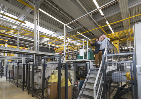 Zwei Männer unterhalten sich in einer Fabrikhalle, lizenzfreies Stockfoto