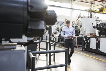 Man with tablet walking in factory shop floor - DIGF01889