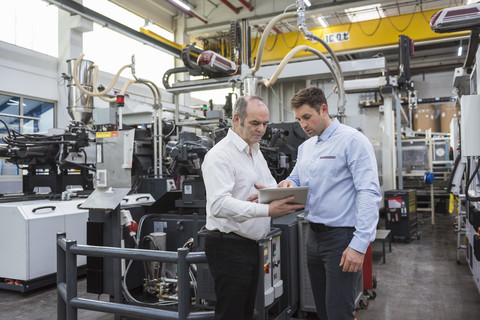 Two men with tablet talking in factory shop floor stock photo