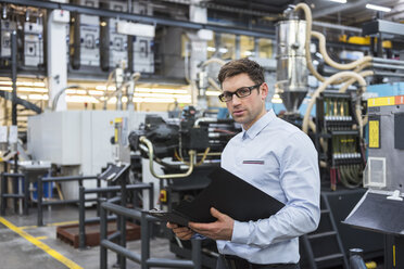 Porträt eines Mannes mit Dokumenten in einer Fabrikhalle - DIGF01903