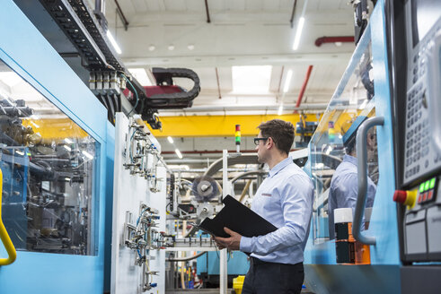 Mann mit Dokumenten zwischen Maschinen in einer Fabrikhalle stehend - DIGF01906