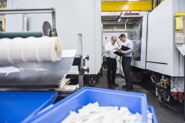 Zwei Männer unterhalten sich zwischen Maschinen in einer Fabrikhalle - DIGF01907