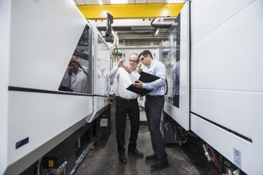 Two men talking among machines in factory shop floor - DIGF01908