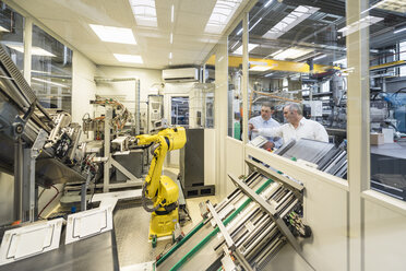 Two men talking in factory shop floor looking at industrial robot - DIGF01941