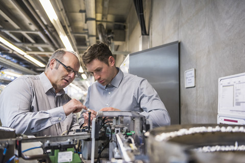 Two men in factory shop floor examining outcome of a machine stock photo