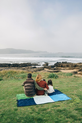 Back view of family with dog sitting on blanket at the coast stock photo