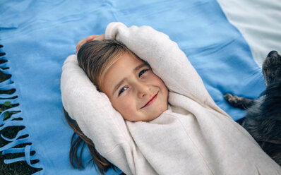 Portrait of smiling girl lying on blanket with dog - DAPF00699