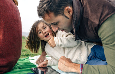 Happy girl and her father using tablet lying on blanket outdoors - DAPF00703