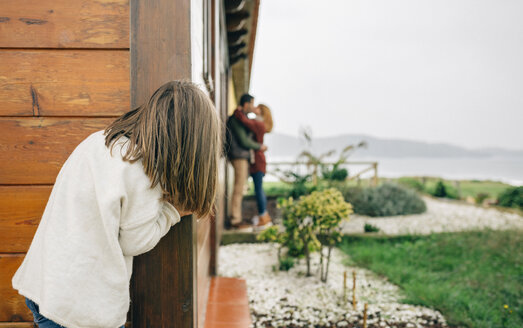 Back view of little girl spying couple in love kissing next to wooden house - DAPF00710