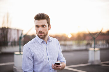 Porträt eines jungen Mannes mit Mobiltelefon, der in die Ferne schaut - DIGF02016