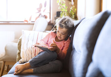 Kleines Mädchen benutzt sitzendes Tablet, sitzend auf Couch - HAPF01490