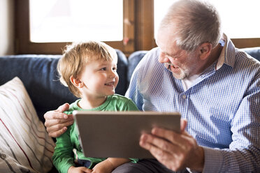 Großvater und Enkel sitzen auf der Couch und benutzen ein digitales Tablet - HAPF01491