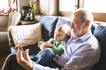 Großvater und Enkel sitzen auf der Couch und benutzen ein digitales Tablet - HAPF01492