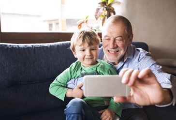 Grandfather and grandson sitting on couch,taking smartphone selfies - HAPF01493