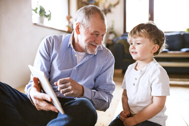 Großvater und Enkel sitzen auf dem Boden und benutzen ein digitales Tablet - HAPF01509