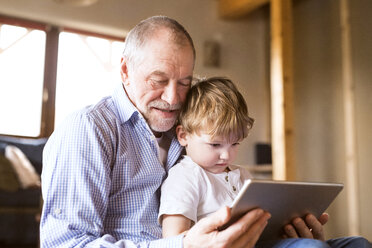 Großvater und Enkel sitzen auf dem Boden und benutzen ein digitales Tablet - HAPF01510