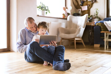 Großvater und Enkel sitzen auf dem Boden und benutzen ein digitales Tablet - HAPF01511