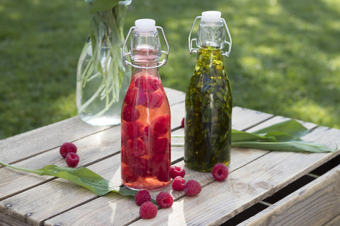 Bügelverschlussflaschen mit gehacktem Bärlauch in Olivenöl und Himbeeren in Weinessig, lizenzfreies Stockfoto