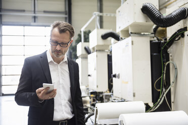 Businessman in factory shop floor looking on the phone - DIGF02020