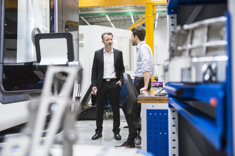 Zwei Männer unterhalten sich in einer Fabrikhalle, lizenzfreies Stockfoto