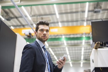 Businessman in factory shop floor holding cell phone - DIGF02043