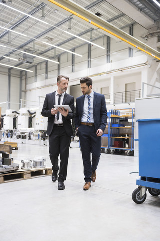 Two businessmen with tablet walking in factory shop floor stock photo