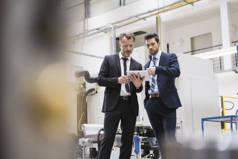 Zwei Geschäftsleute teilen sich ein Tablet in einer Fabrikhalle - DIGF02047