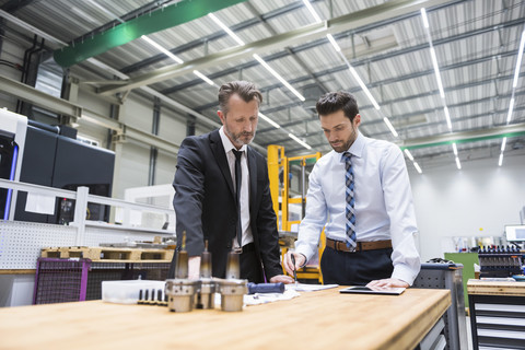 Two businessmen at table in factory shop floor examining product stock photo