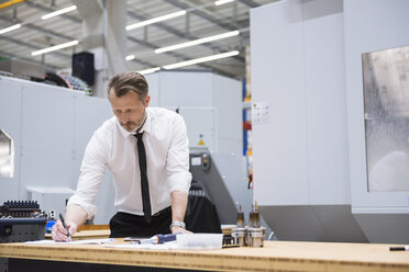 Mann am Tisch in der Fabrikhalle macht sich Notizen - DIGF02055