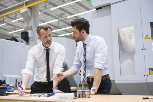 Two businessmen at table in factory shop floor discussing - DIGF02056