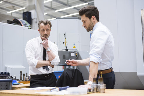 Two businessmen at table in factory shop floor discussing - DIGF02057