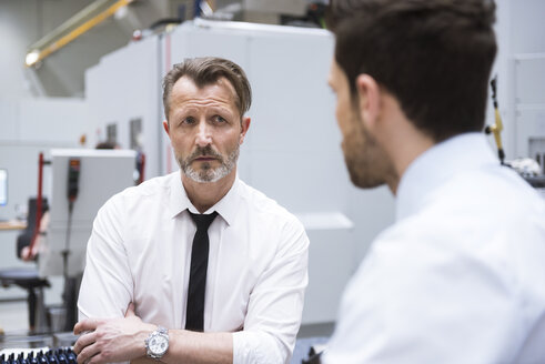 Businessman in factory looking at colleague - DIGF02058