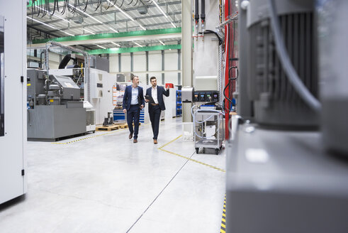 Two men walking and talking in factory shop floor - DIGF02069