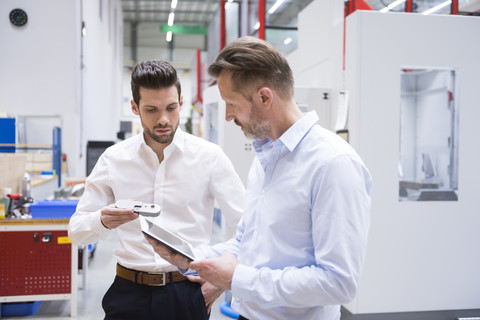 Two men with tablet and product in factory shop floor stock photo