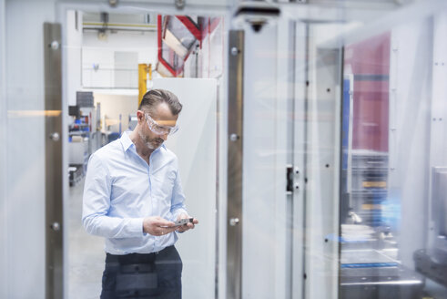 Mann mit Schutzbrille in einer Fabrik, der ein Produkt hält - DIGF02080