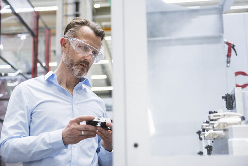 Man wearing safety goggles in factory holding product - DIGF02082