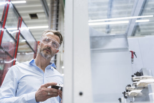 Man wearing safety goggles in factory holding product - DIGF02083