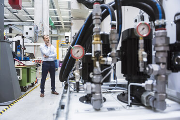 Mann in Fabrikhalle mit Blick auf eine Maschine - DIGF02085