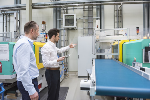 Zwei Männer in einer Fabrik sprechen an einer Maschine, lizenzfreies Stockfoto