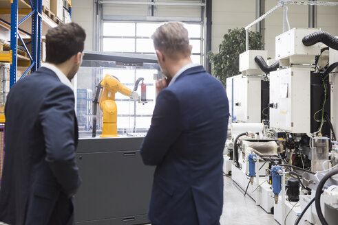 Two businessmen in factory shop floor looking at industrial robot - DIGF02096